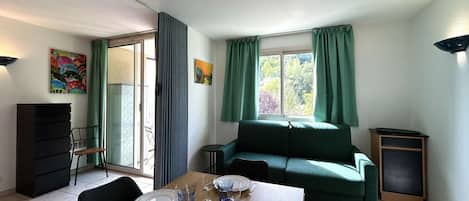 Un coin repas avec une table dressée pour quatre personnes, un canapé vert et une fenêtre avec des rideaux.