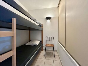 A small, narrow room with a bunk bed, a single chair, and a wall-mounted light fixture. - Cozy 2-Room Cabin Apt. for 4 - Near Prorel Cable Car & Briançon Center (Briançon)