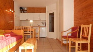 A cozy room with a bed, a wooden table, two chairs, a kitchen area with cabinets, and a door leading to another room. - 2-room apartment night area, parking, wifi - Briançon (Briançon)