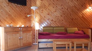 A cozy attic bedroom with a wooden slat ceiling, a bed with red bedding, a wooden dresser, and a floor lamp. - 2-room apartment night area, parking, wifi - Briançon (Briançon)