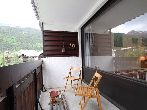 A balcony with two wooden chairs, a small table, and a red tray with cups and a bowl.