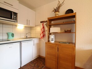 Una cocina compacta con microondas, hervidor, cafetera y un armario de madera con estantes.