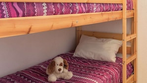 Una cama litera con un edredón estampado y un peluche de perro en la cama inferior.