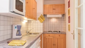 Cocina compacta con microondas, cafetera, lavabo y armarios de madera.
