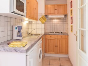 Cocina compacta con microondas, cafetera, lavabo y armarios de madera.