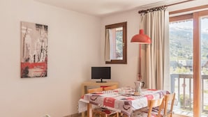 Un comedor con una mesa lista para dos personas, un televisor y vistas a un paisaje montañoso a través del ventanal.