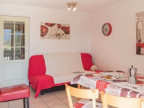 Una habitación acogedora con un sofá rojo, una mesa de comedor con mantel de 'caffe', un reloj y un cuadro de flores.