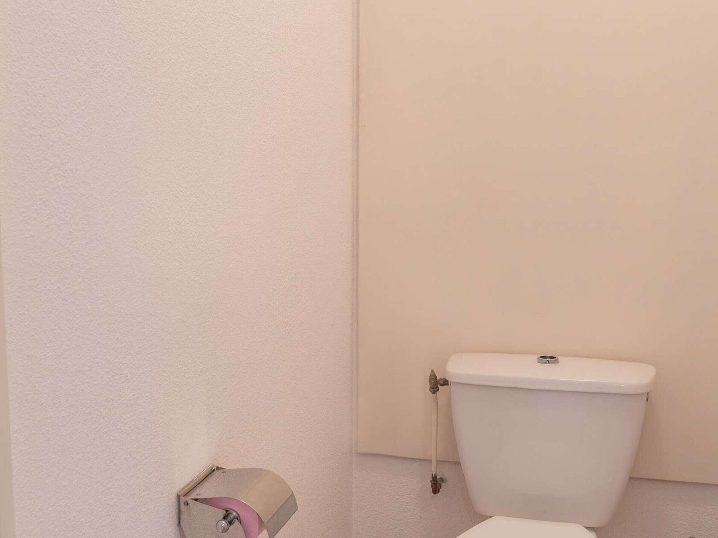 A bathroom with a toilet, a roll of toilet paper, and a wall-mounted towel dispenser.