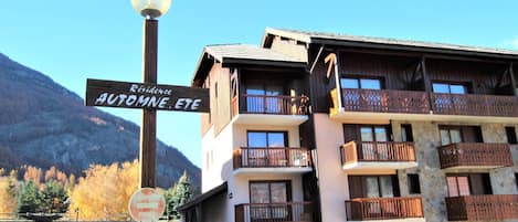 Un edificio de varios pisos con balcones, un letrero que indica 'Residence AUTOMNE. ETE' y una señal de no estacionamiento.