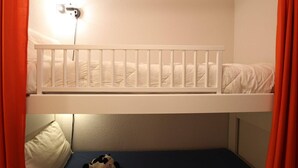 A bunk bed with a white frame and mattress, a bedside table with a lamp, and a toy cow on the lower bed.