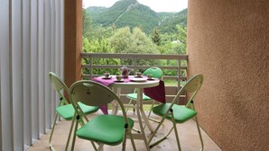 A balcony with a table and chairs, overlooking a mountainous landscape.