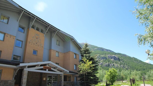 A building with a stone entrance, a sign reading "Hotel", and a mountain backdrop.