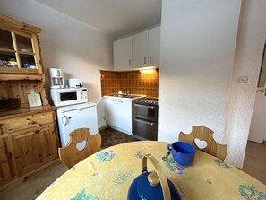A compact kitchen with white appliances, a wooden cabinet, and a table with a floral tablecloth.