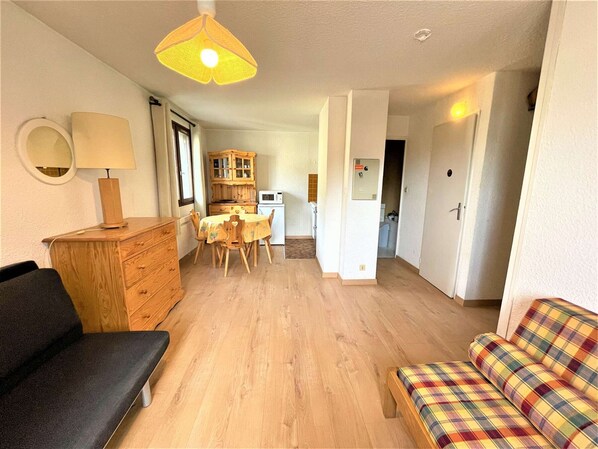 Una sala de estar acogedora con un sofá, una mesa de comedor con sillas, un armario de madera y una pequeña cocina.
