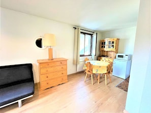 A compact living space with a sofa, wooden dresser, dining table with chairs, a microwave, and a cabinet. - Cozy Studio with Mountain Corner - 4 Sleeps, Near Slopes & Shops, La Salle Les Alpes (La Salle-les-Alpes)