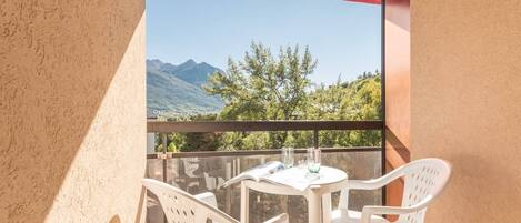 A balcony with a table and chairs, a red awning, and a view of mountains and trees.