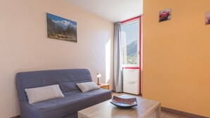 A room with a blue sofa, a wooden coffee table, a picture of mountains, and a window with a view of a mountain. - Cozy studio 2/4 pers, Near Prorel lift and center (Briançon)