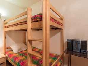 Un lit superposé avec une couverture à carreaux et un oreiller. Une petite table de chevet en bois se trouve à côté du lit.
