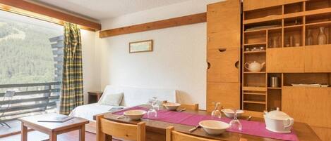 A cozy room with a wooden dining table set for four, a bed with white linens, and a large wooden cabinet with shelves.