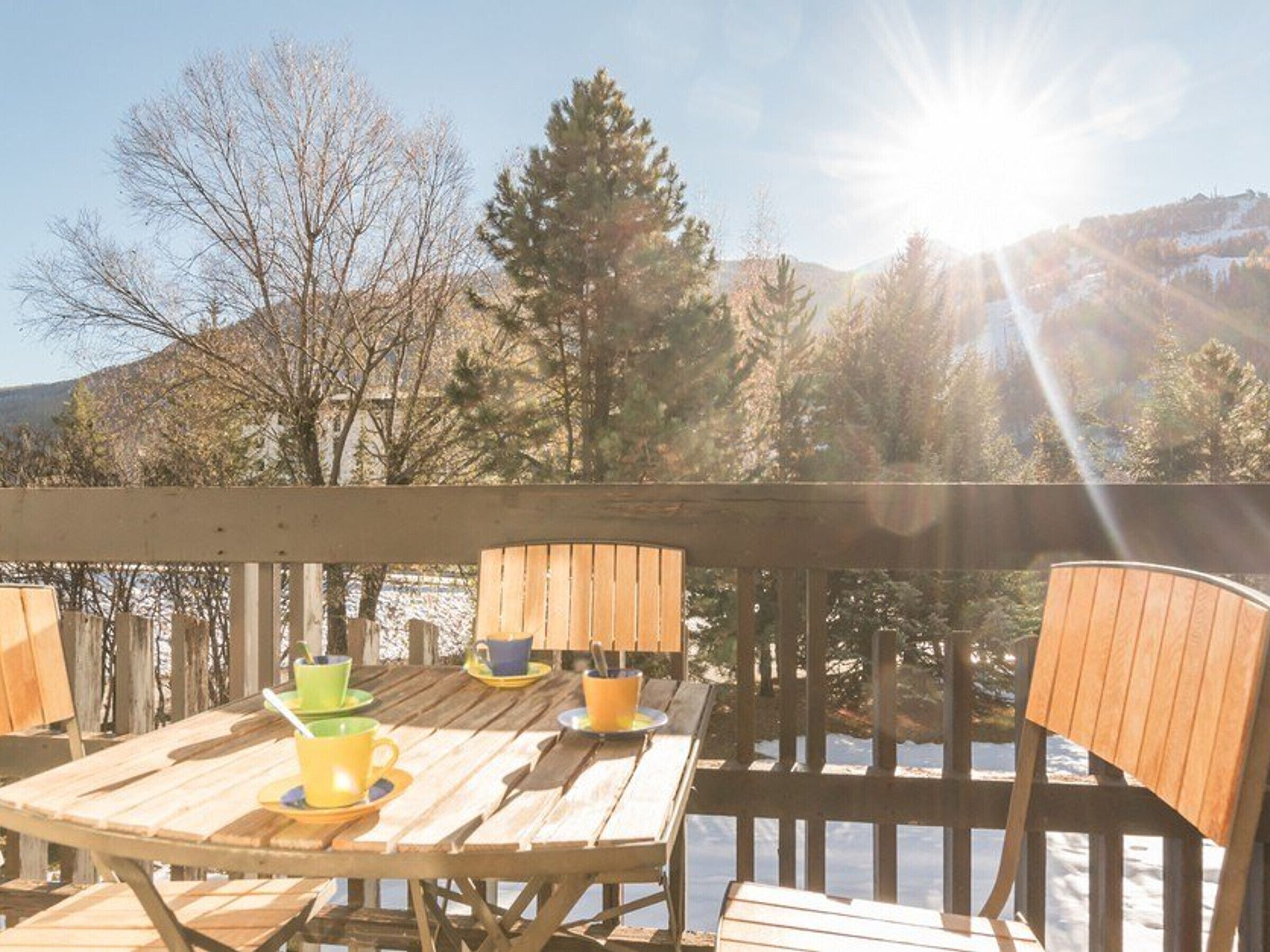A wooden deck with a table and chairs, overlooking a mountainous landscape.