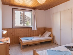 A small, cozy room with a wooden bunk bed, a desk with a lamp, and a window with a view of buildings. - Spacious 4-Room Apartment for 7 in Serre-Chevalier, Chantemerle - Balcony & Parking Included (Saint-Chaffrey)