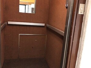 Un ascensor estrecho con puerta metálica y un pequeño ventanal en la parte superior.