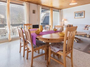 A dining area with a wooden table and chairs, a purple tablecloth, and a view of the outside through large windows. - Spacious 4-Room Apartment for 7 in Serre-Chevalier, Chantemerle - Balcony & Parking Included (Saint-Chaffrey)