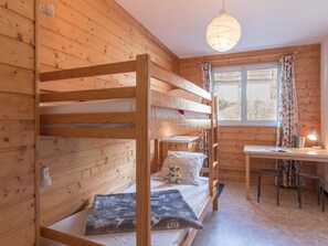 Habitación con literas, un escritorio, una silla, paredes de madera y una ventana con cortinas.