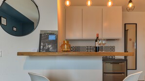 Una cocina moderna con encimera de madera, dos sillas blancas, un espejo redondo e iluminación colgante.