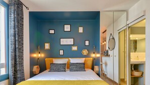 Un dormitorio con cama, mesitas de noche, armario y baño a la vista a través de una puerta abierta.