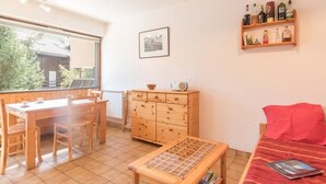 A room with a wooden dining table and chairs, a small wooden cabinet, a red sofa, and a shelf with bottles. - Cozy mountain studio for 5 people in Chantemerle - Serres-Chevalier (Saint-Chaffrey)