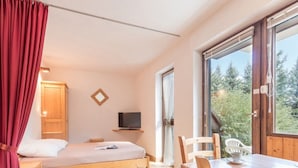 A bedroom with a bed, a TV, a wooden wardrobe, a window, and a dining area with chairs and a table. - Cozy mountain studio for 5 people in Chantemerle - Serres-Chevalier (Saint-Chaffrey)