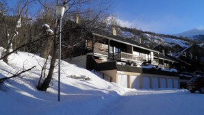 A snow-covered building with a balcony, a street lamp, and a mountain in the background. - Cozy mountain studio for 5 people in Chantemerle - Serres-Chevalier (Saint-Chaffrey)