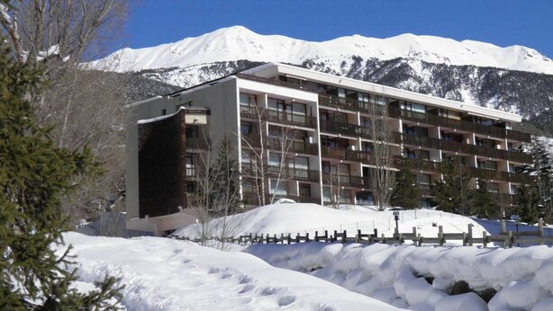 Un hôtel à plusieurs étages, doté d’une architecture moderne, situé dans une région montagneuse enneigée, sous un ciel dégagé.