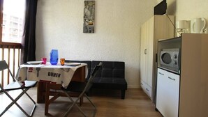 Un espace de vie compact comprenant un coin cuisine, un coin repas avec une table et des chaises, un canapé et une fenêtre avec des rideaux.