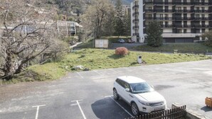 Un espace de stationnement avec un VUS blanc, un immeuble à plusieurs étages doté de balcons et un paysage montagneux en arrière-plan.