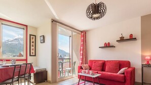 A living room with a red sofa, a dining table with chairs, a balcony with a view of a mountain, and a red lamp. - 2-room apartment with balcony, near slopes - Briançon (Briançon)