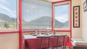 A dining area with a table set for two, a window with a mountain view, and a small seating area with a cushion. - 2-room apartment with balcony, near slopes - Briançon (Briançon)