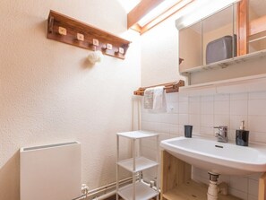 Une salle de bain avec un lavabo blanc, une étagère en bois sur laquelle est posée une serviette, et un miroir au-dessus du lavabo.