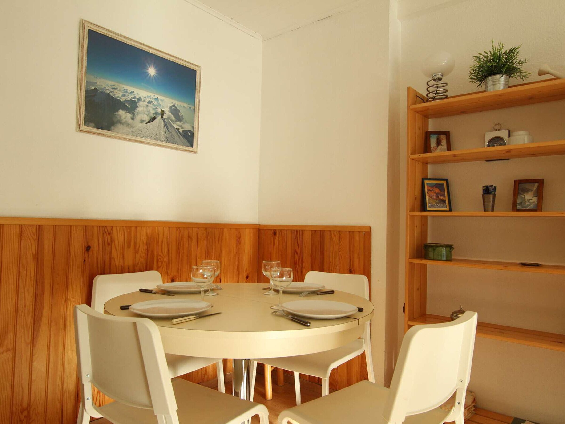 A dining area with a round table set for four, white chairs, and a wooden panel wall.