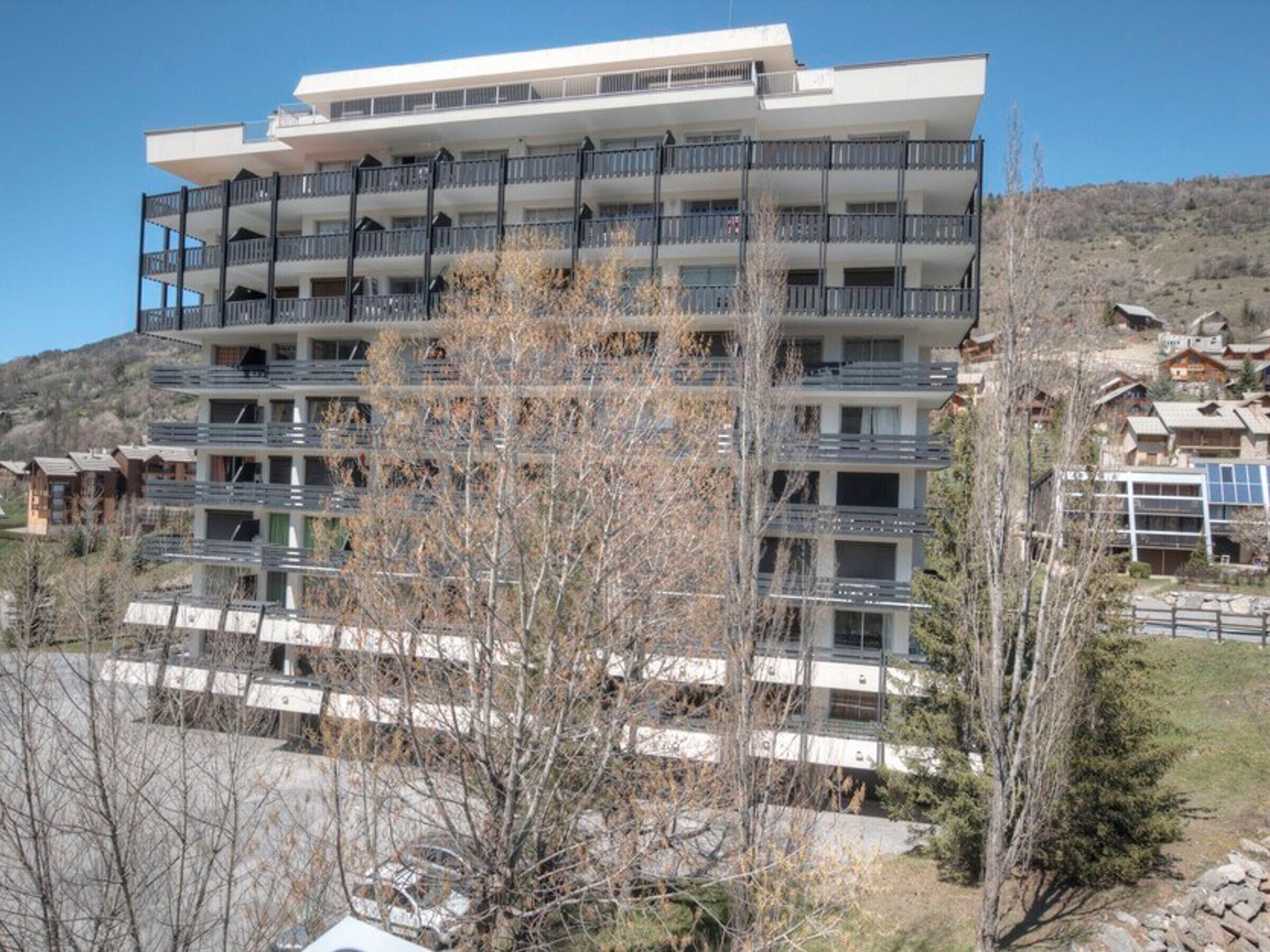 A multi-story hotel with balconies, a flat roof, and a view of a mountainous area.