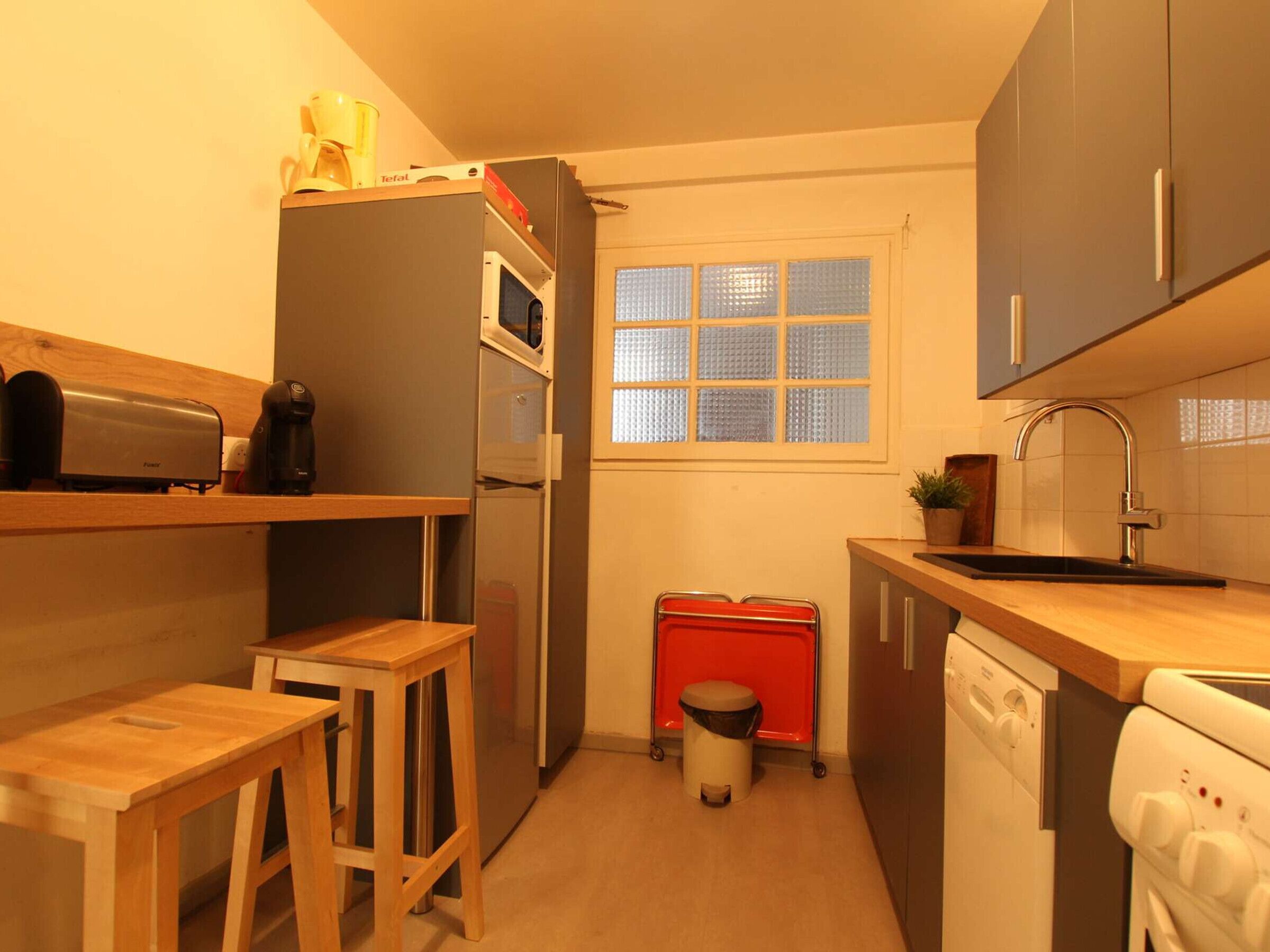 Een kleine keuken met een koelkast, magnetron, spoelbak en houten krukken.