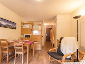 A compact room with a dining table, chairs, a kitchenette, a bunk bed, and a single chair with a blanket. - Ski-In Studio with Mountain View, Pool, and Garden Access in La Salle-les-Alpes (La Salle-les-Alpes)