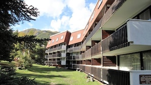 A multi-story building with balconies, surrounded by greenery and mountains.