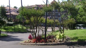 A landscaped area with trees and shrubs, a paved road, and a building with a tiled roof in the background. - Apartment in a residential leisure *** for 4 people (Moliets-Et-Maa)