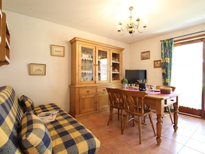 Una sala de estar acogedora con un sofá a cuadros, una mesa de comedor de madera y un mueble con puertas de cristal.