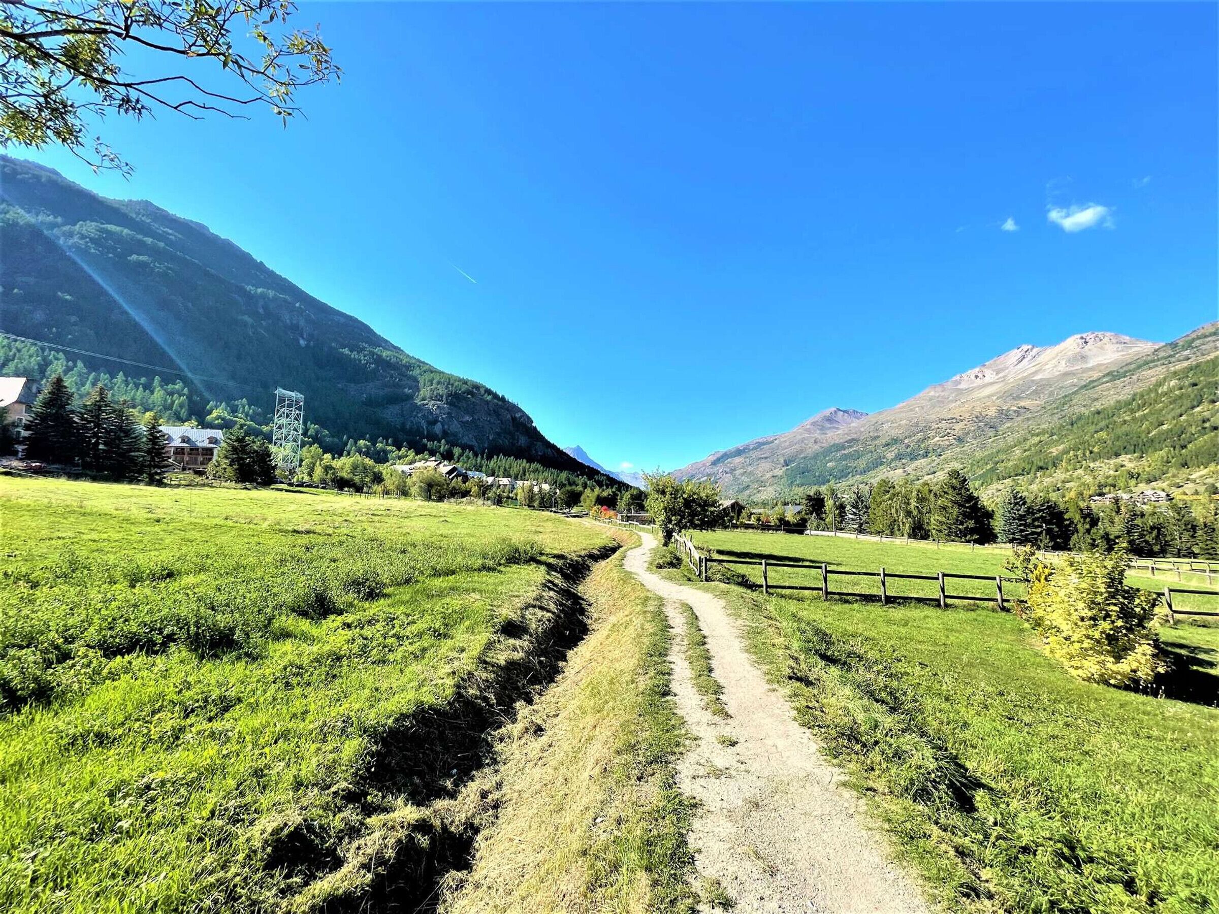 A rural landscape with a dirt path, green fields, and mountains in the background.