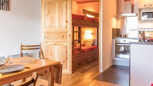 A compact room with a bunk bed, a wooden dining table, and a kitchenette. - Renovated studio near slopes, parking, equipped kitchen (La Salle-les-Alpes)