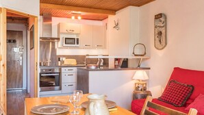 A cozy kitchen with modern appliances, a dining table set for two, and a red sofa in the living area. - Renovated studio near slopes, parking, equipped kitchen (La Salle-les-Alpes)