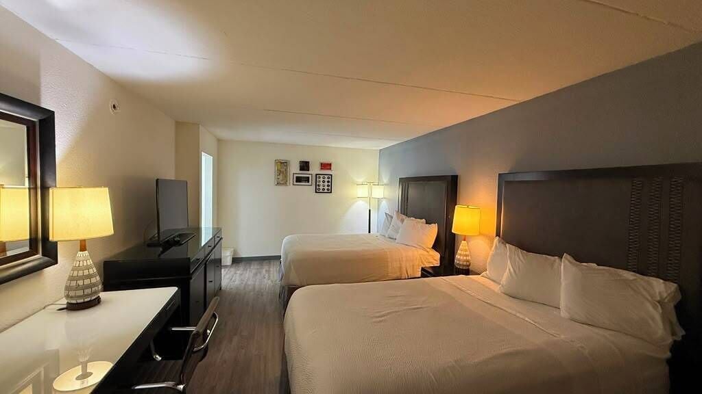 Habitación de hotel con dos camas, un escritorio, una silla, un televisor y una lámpara.